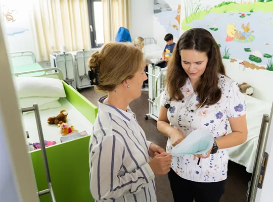 A teacher and a parent stand in a cheerfully decorated hospital room